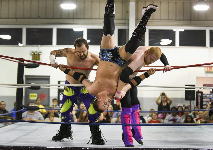 Randall Shane, left, and B-wood, right, throws The System, middle, out of the ring during their match. Michael Noble Jr./HERALD