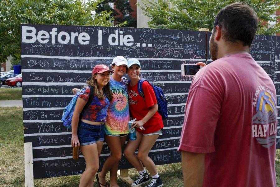Versailles freshman Rebekah Alvey, left, Loretto freshman Kelly Peterson, center, and Owensboro freshman Sophia Blair, right, take a picture in front of the Before I Die wall during the Happy Daze event hosted by ATO on Friday, Sept. 9 outside of Downing Student Union.