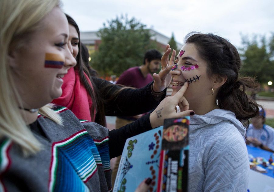 Princeton junior Kate Hart, left, and Bowling Green junior Cindy Gomez apply stickers onto Tell City, Indiana, sophomore Mercedes Mendez at the Hispanic Heritage Festival on Thursday, Oct. 13, at Centennial Mall. The stickers resemble face paintings traditionally worn on Day of the Dead, a Mexican holiday celebrated every October. Mendez takes pride in her Mexican heritage and said she wants to share her culture with others. 