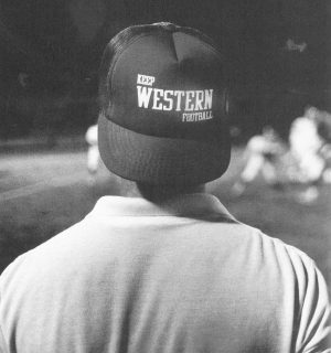 Sporting a hat that mirrored the attitudes of many Western football fans, Daily News Sports Editor Joe Medley watches the Red-White scrimmage game from the sidelines.