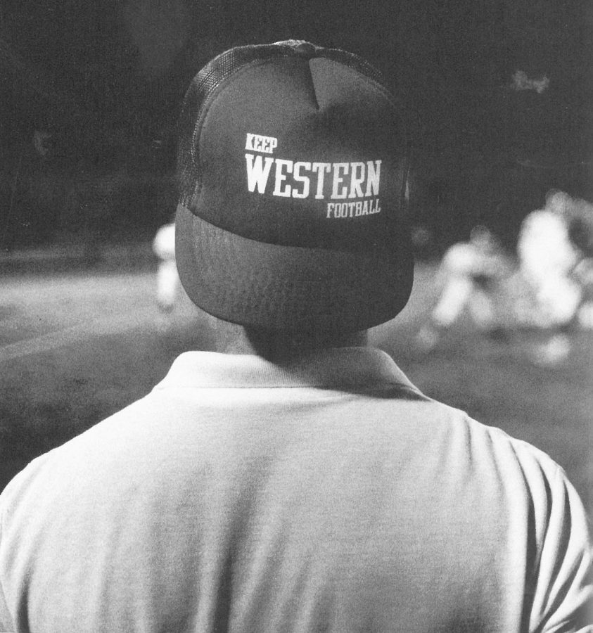 Sporting a hat that mirrored the attitudes of many Western football fans, Daily News Sports Editor Joe Medley watches the Red-White scrimmage game from the sidelines.