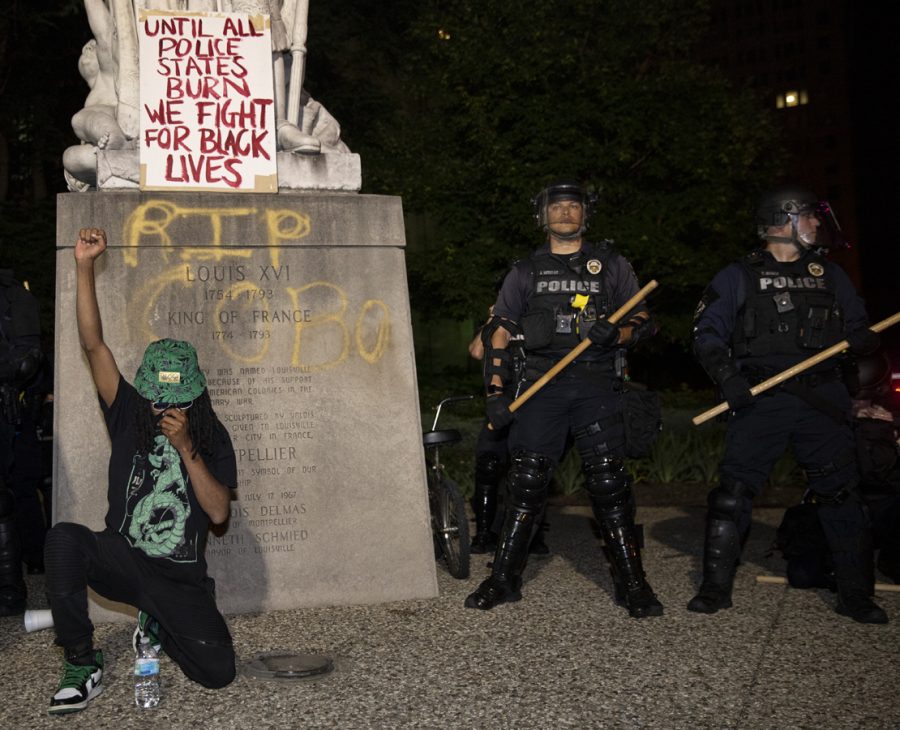 A young protestor displays a raised fist while taking a knee in front of a vandalized statue of Louis XVI at Louisville City Hall. Both gestures have become popular symbolic acts of protest against racism.