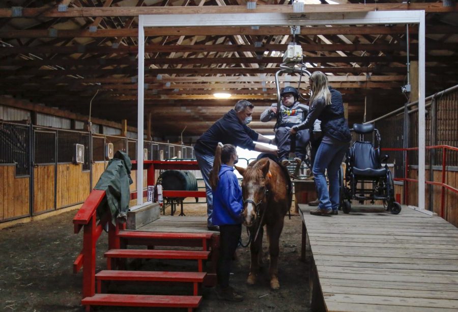 Staff members and volunteers help student rider Ben from his wheelchair to Leroy the horse before the start of a lesson. Riding lessons at New Beginnings act as both a fun activity for students as well as therapy sessions.