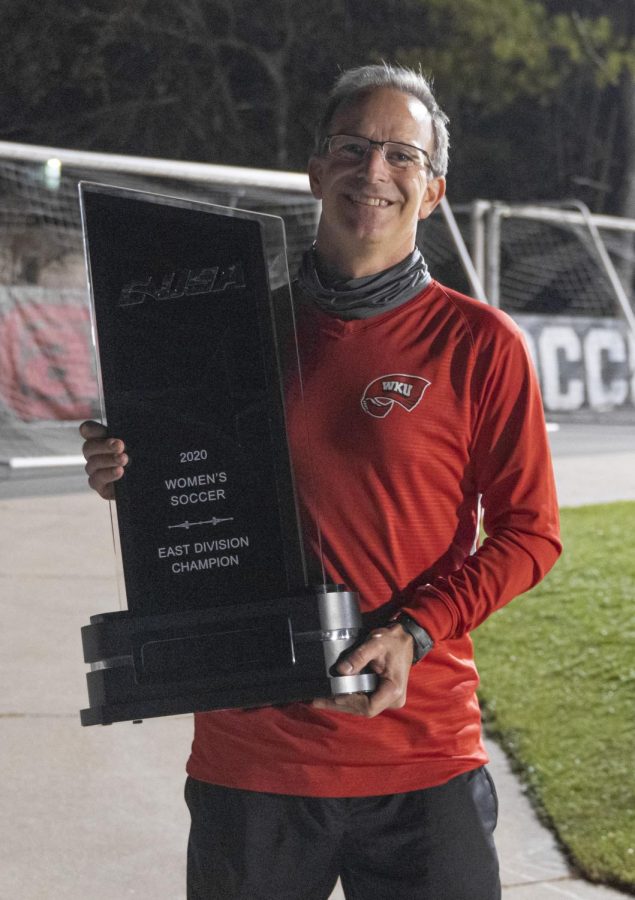 WKU soccer head coach Jason Neidell holding the first C-USA East Division title trophy in program history. Neidell has been the programs only coach in the teams existence. 