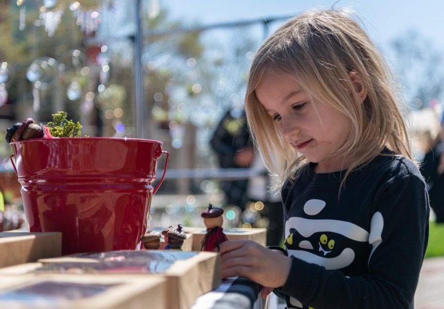 Petra Fulkerson, 5, daughter of Lisa Fulkerson, 34, plays with an acorn-doll on sale at the stall for their business, P & M Farms, on Wednesday, March 29, 2023 during the Market on the Avenue event held at Centennial Plaza on the WKU campus in Bowling Green, Ky.