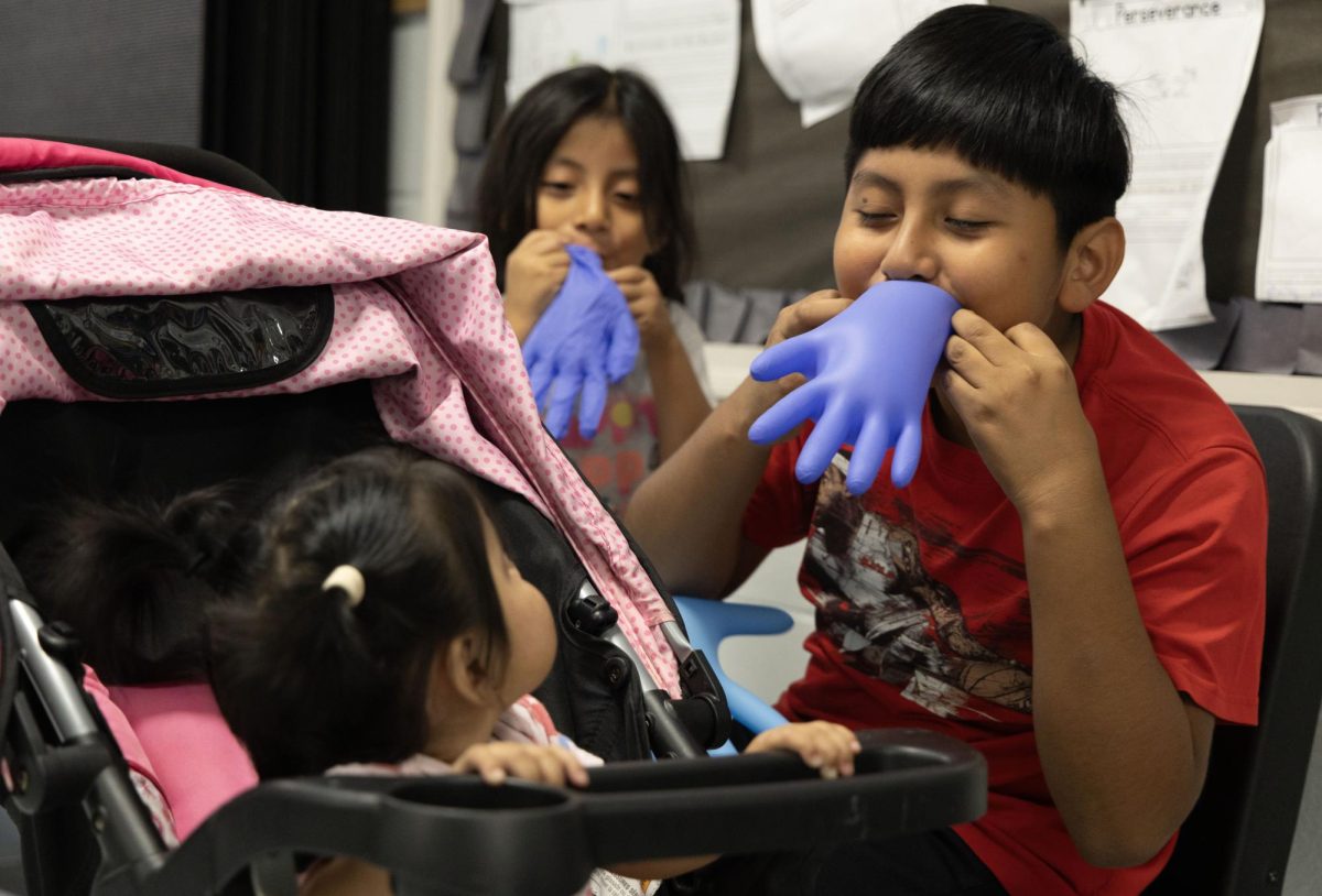 11-year-old Brian Siles and 5-year-old Daisy Siles entertain Nallely Siles, 1, with balloons made from rubber gloves during a Remote Area Medical (RAM) clinic at Teranga Academy on Aug. 26, 2023. The event was the first time a RAM clinic has been hosted in Bowling Green.
