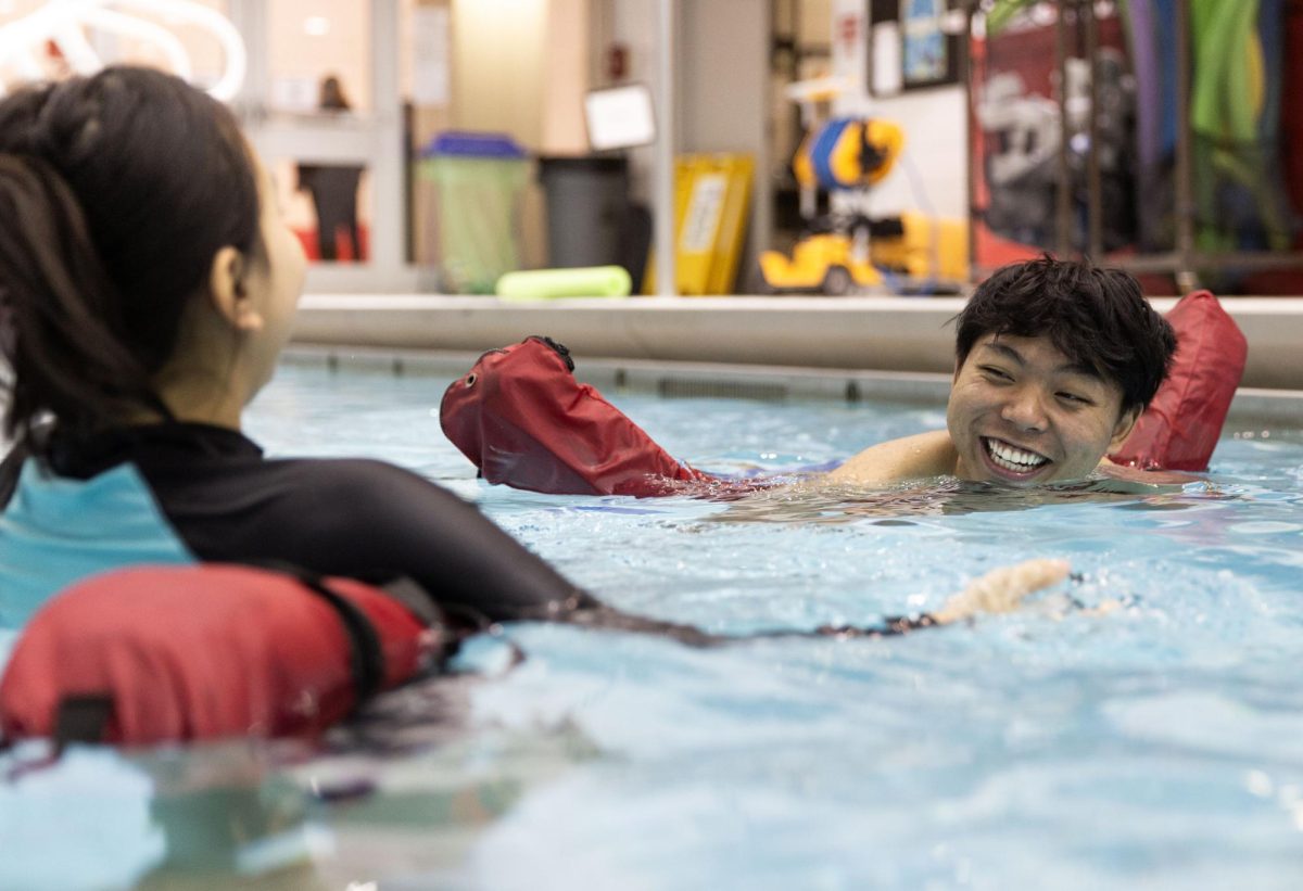 Au Reh (right) and Pha Meh (left) laugh at each other while learning to paddle on their flotation devices at their first swimming lesson in the Bill Powell Natatorium at Western Kentucky University in Bowling Green Ky. On Feb. 28, 2024.