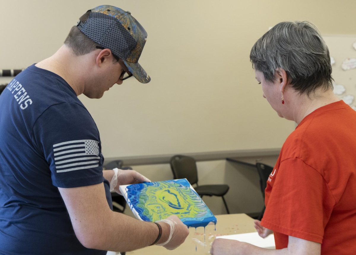 WKU mental health provider and licensed clinical social worker Mariya Fye examines an attendees acrylic pour painting during the Therapeutic Art Night event hosted by WKU Military Student Services and WKU Counseling Center on April 17, 2024.