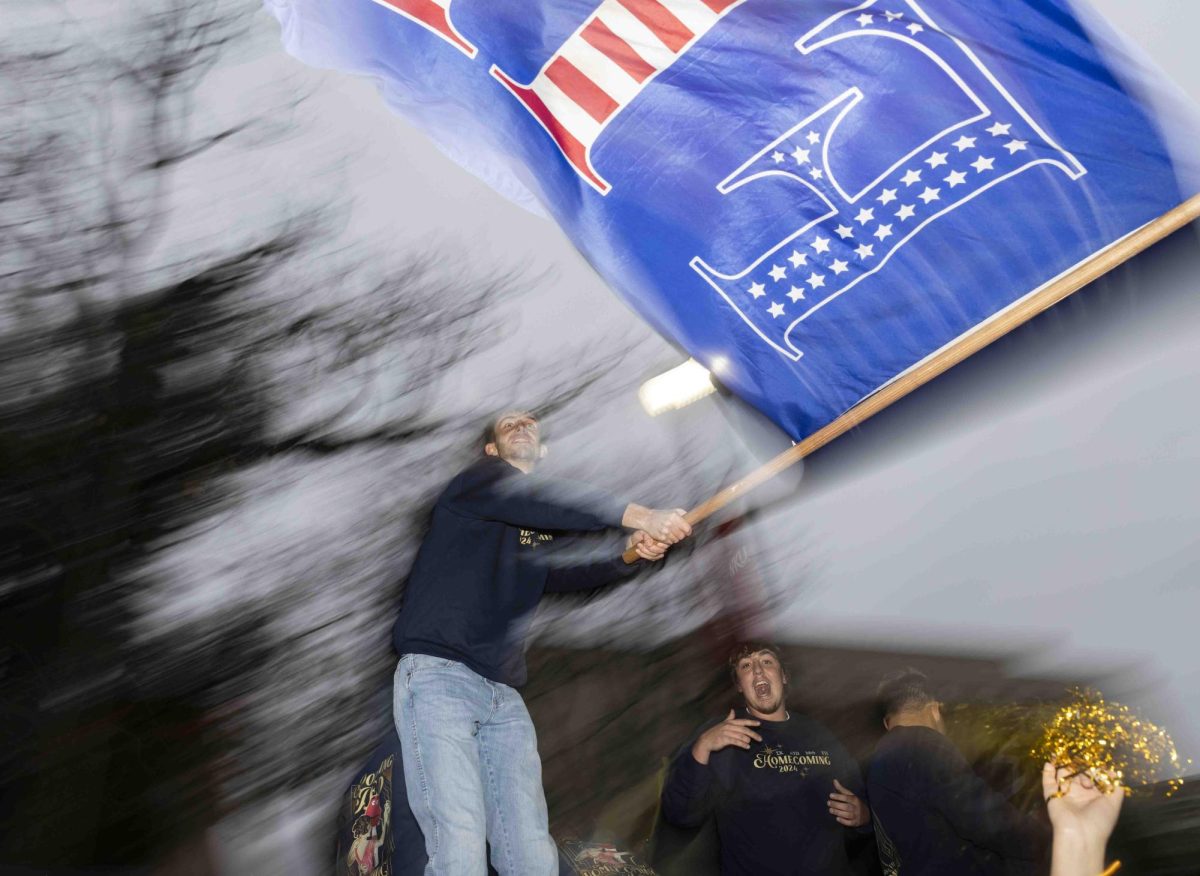 Farmhouse sophomore Caleb Hochgesang waves a flag above his fraternity’s float before the homecoming parade on Friday, Nov. 15, 2024.