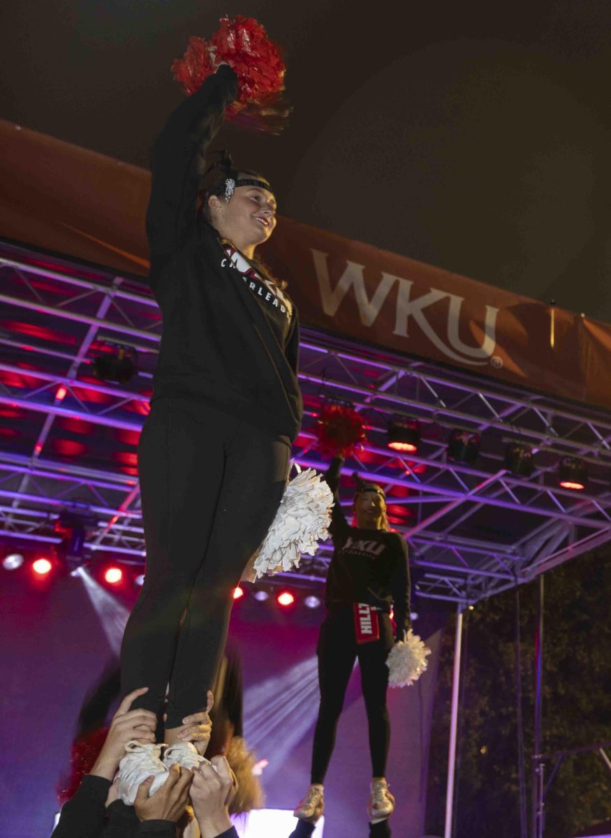 A WKU cheerleader waves at the crowd in front of the Big Red Roar after the homecoming parade on Friday, Nov. 15, 2024.