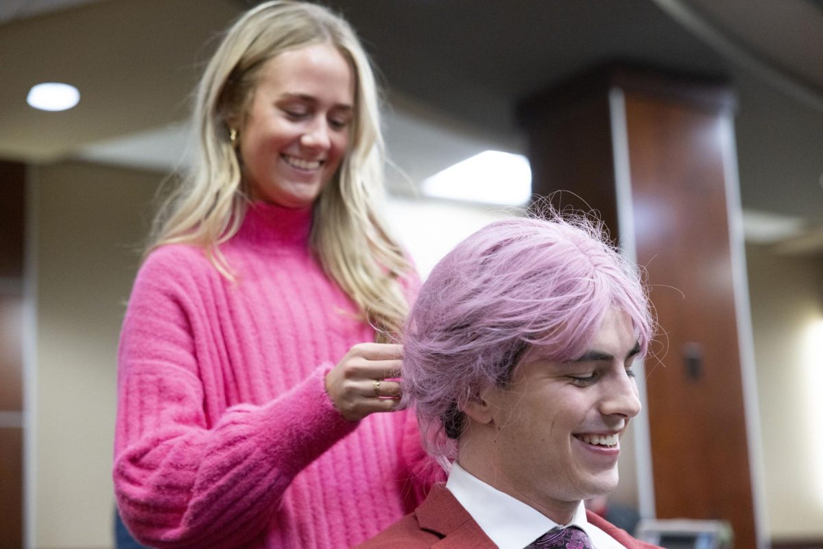 Student Body President Sam Kurtz has his pink wig put in bun by Chief of Staff Anne-Marie Wright ahead of the Student Government Association’s weekly meeting in the senate chambers on Tuesday, Feb. 18, 2025. Multiple members of the SGA wore pink wigs to the meeting in support of breast cancer awareness.