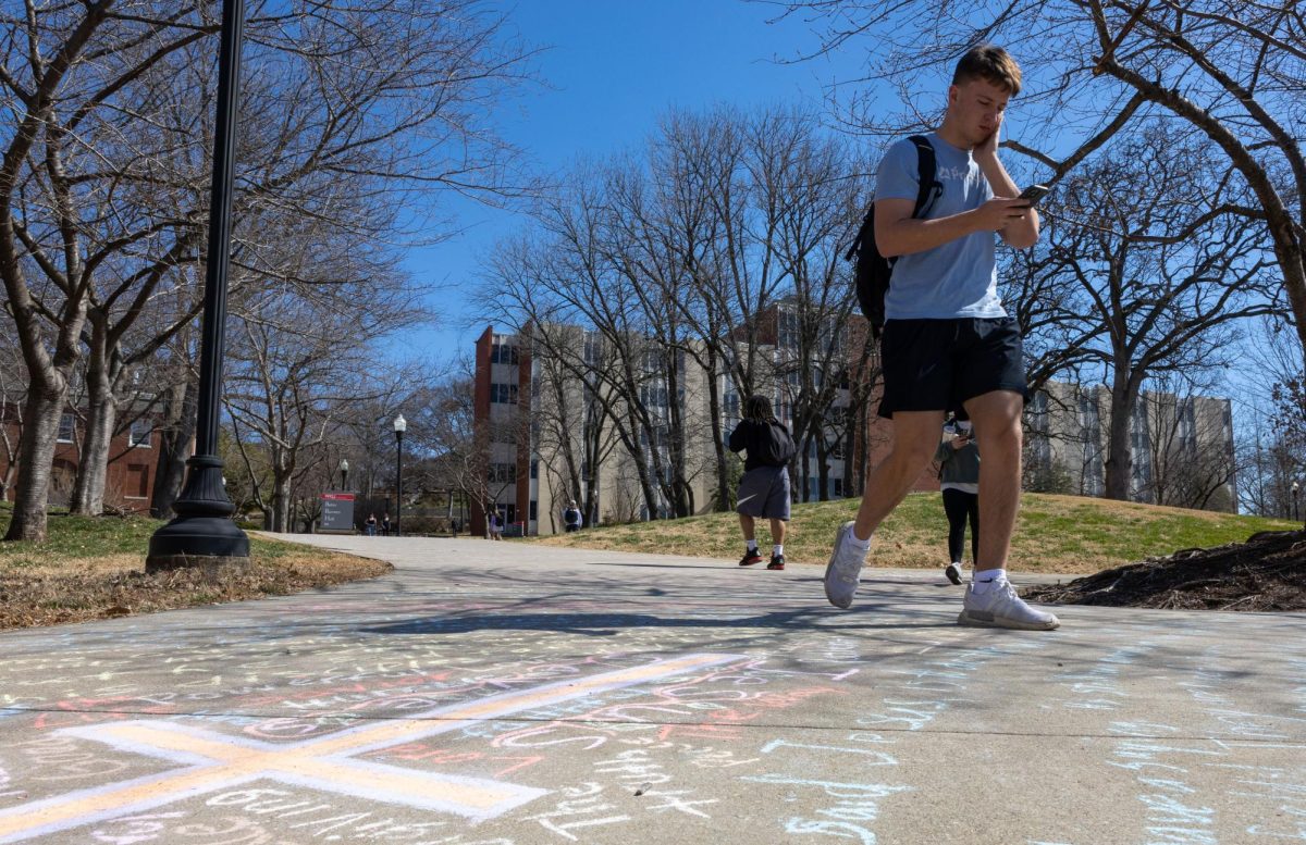 Sophomore Eli Carter walks on the sidewalk with the Gospel of John written on it with chalk near Grise Hall on Monday, March 11, 2025. The night before, various Christian campus ministries came together to write all 21 chapters (879 verses) of the Gospel of John from just outside Grise Hall down to the Preston Health and Activities Center.