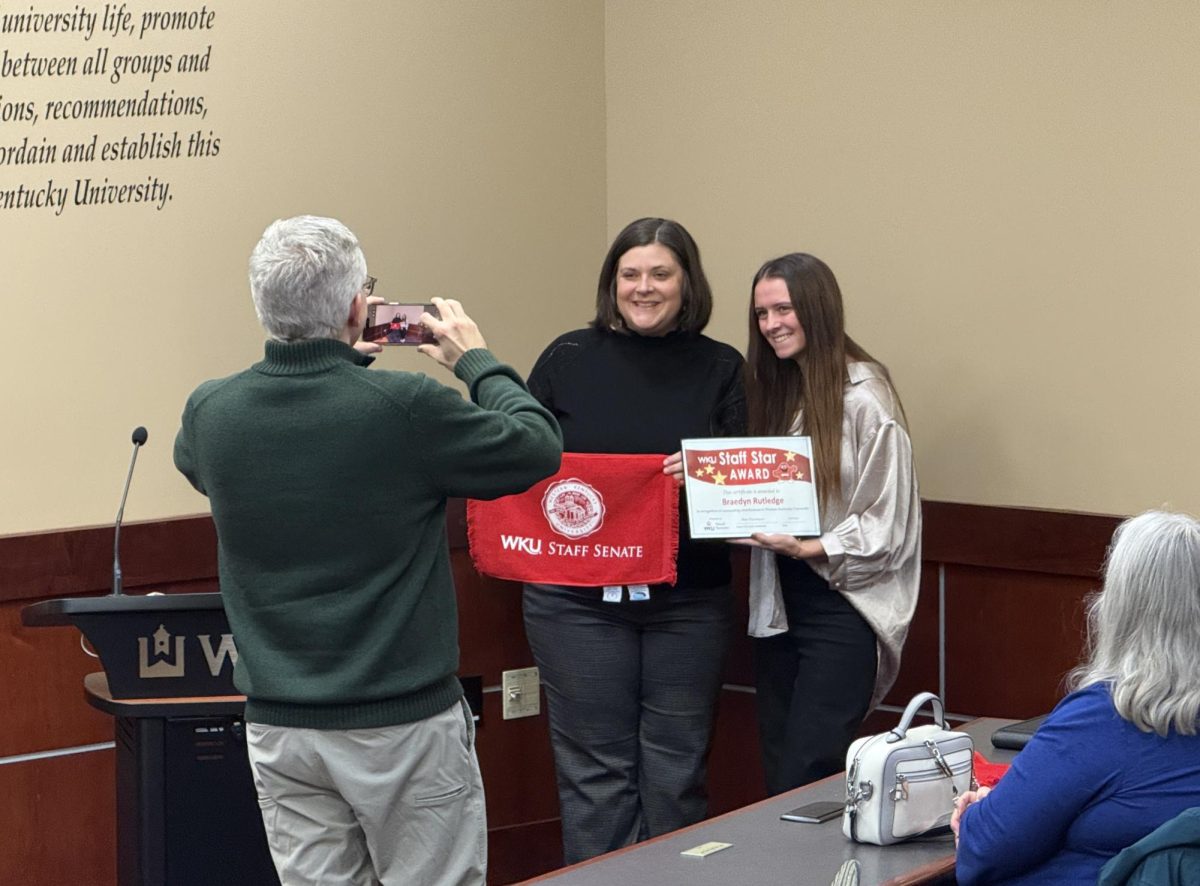 Staff Senate Vice Chair Jordan Ray (left) photographs the College of Health and Human Services’ Senior Academic Advisor Marybeth Hunt (middle) with Staff Star Award Recipient Braedyn Rutledge (right), an academic advisor in the CHHS. Hunt nominated Rutledge for the award and gave remarks at the Staff Senate meeting on Wednesday, Dec. 3, 2025