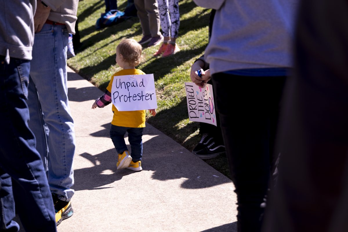 A child, followed closely by their parents, wonders around 
Wasioto Park bearing a sign that reads, “Unpaid Protestor” during the third nationwide “No Kings” protest on Saturday, March 28, 2026 in Nashville, Tenn.