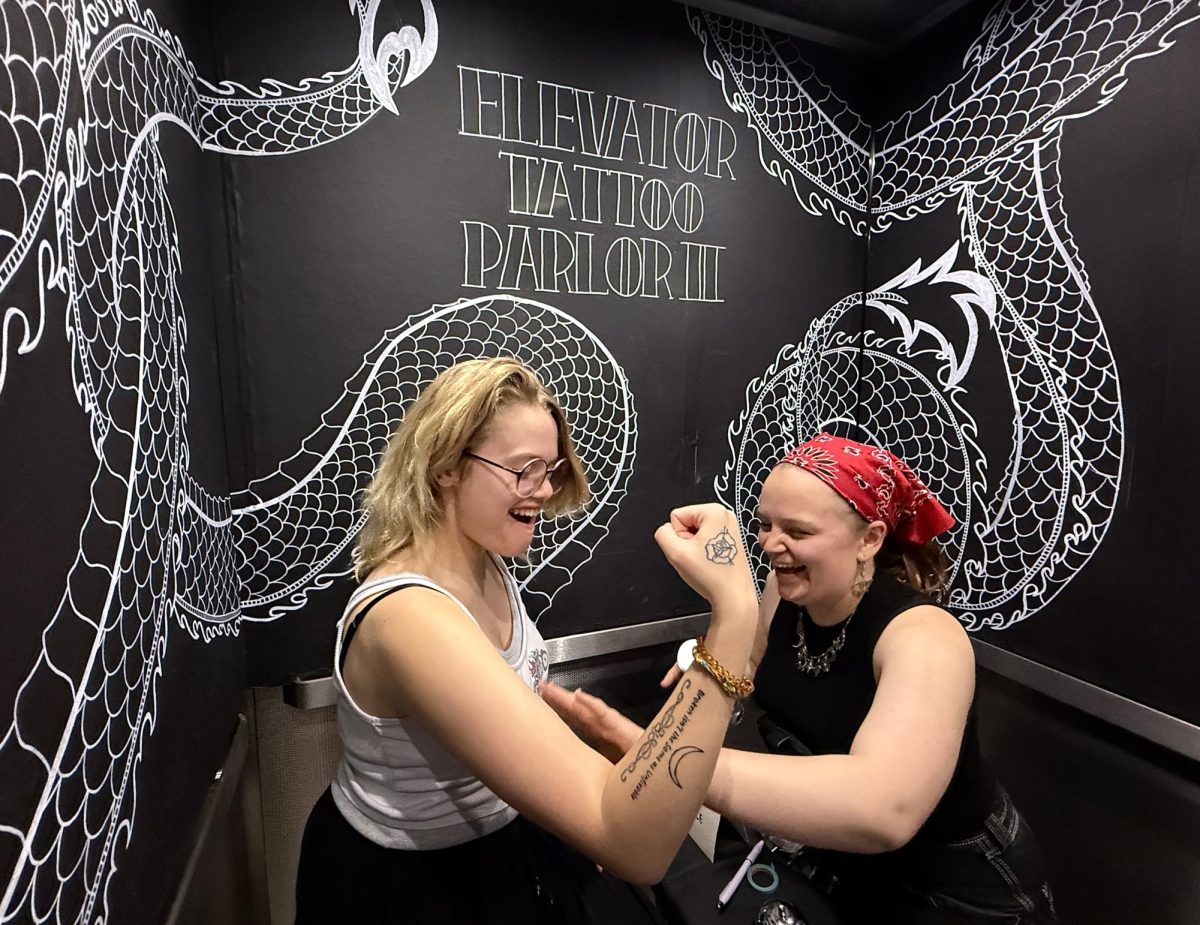 Sav Covey, senior film production major, gets a temporary tattoo done by her roommate Zoe Eckhart, a senior studying for a BFA in sculpture. Covey had her tattoo done at the "Elevator Tattoo Parlor Flash Sale" art installment and performance organized by Eckhart on Wednesday, April 8, 2026.